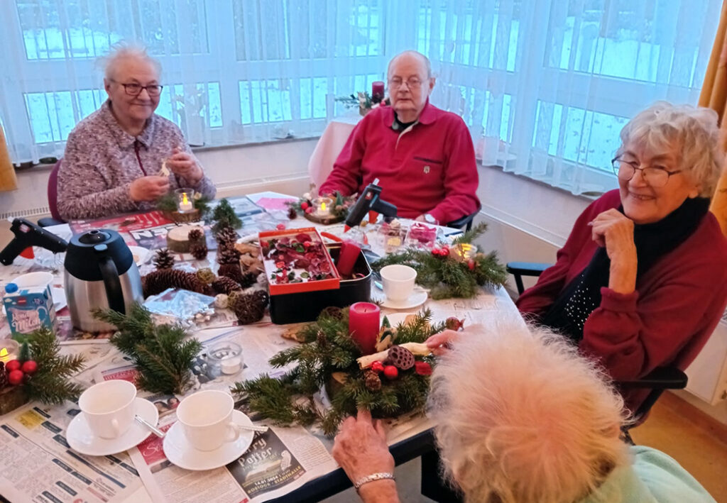 Eine Gruppe von &auml;lteren Menschen sitzt um einen Tisch und bastelt weihnachtliche Dekorationen.