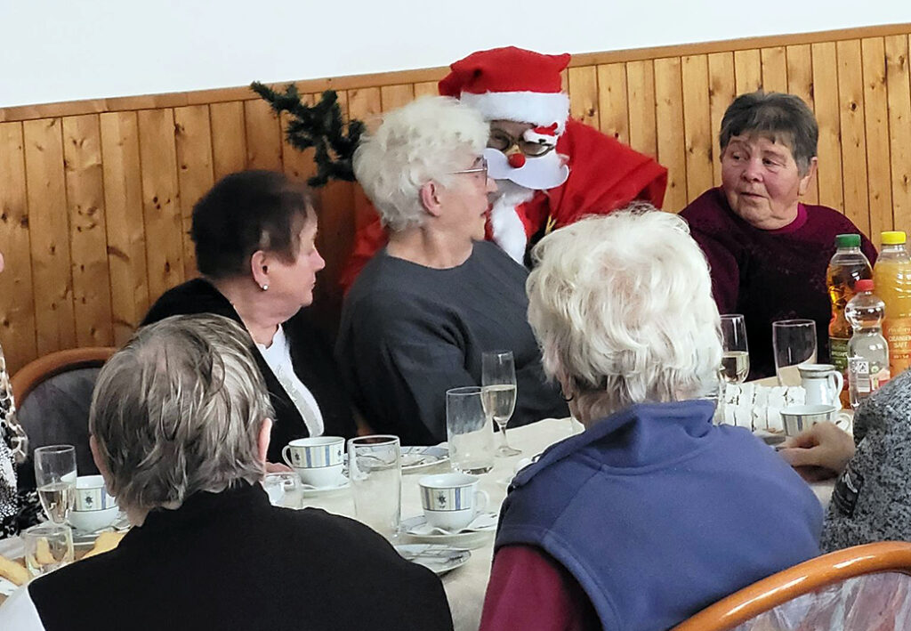 &Auml;ltere Menschen bei einer Weihnachtsfeier, ein als Weihnachtsmann verkleideter Mensch sitzt dabei.