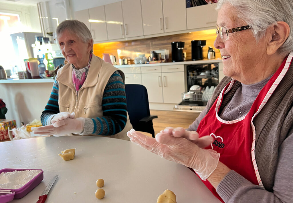 Zwei &auml;ltere Frauen sitzen in einer K&uuml;che und formen Teigkugeln.