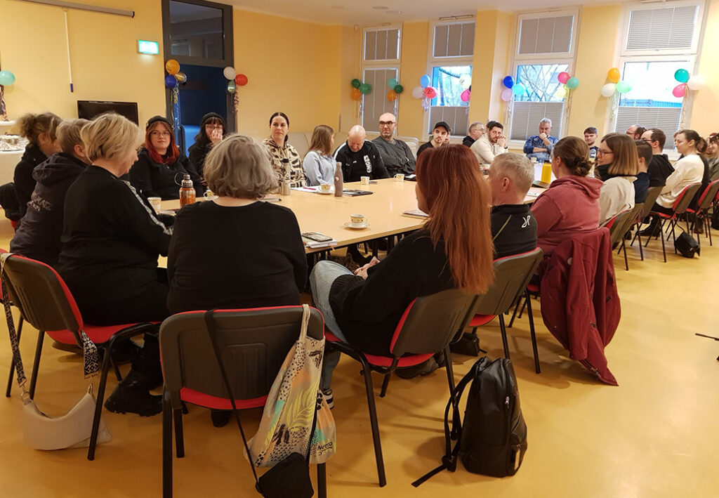 Menschen sitzen in einem Raum um einen gro&szlig;en Tisch und diskutieren.