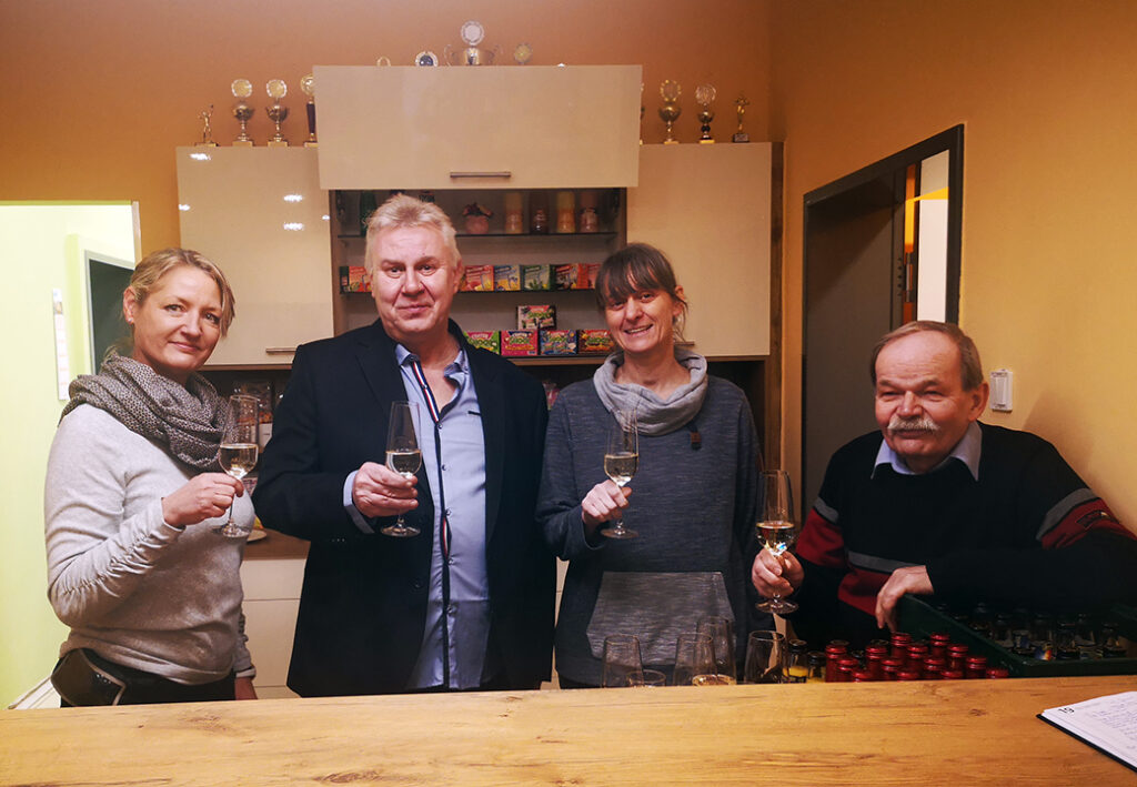 Vier Personen stehen an einem Tresen und halten Weingl&auml;ser in der Hand.