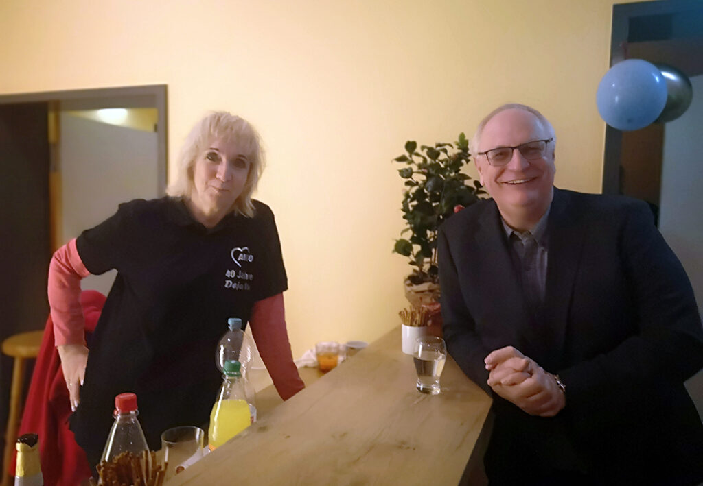 Zwei Personen stehen an einem Tisch und l&auml;cheln.