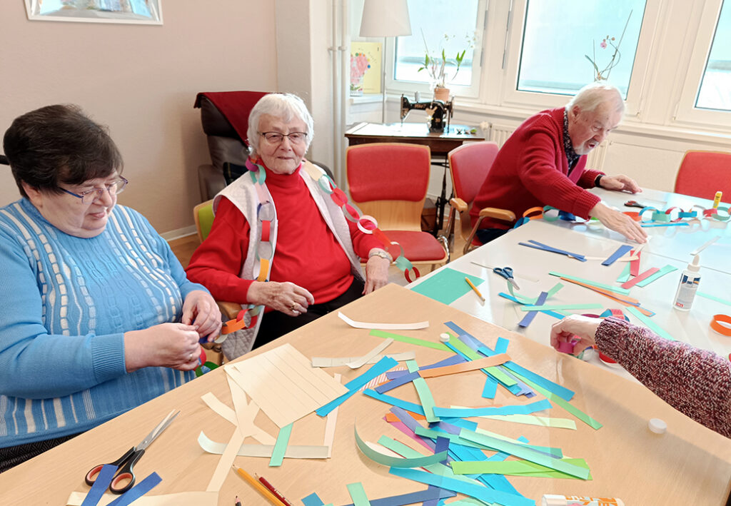 Drei ältere Menschen basteln zusammen an einem Tisch.