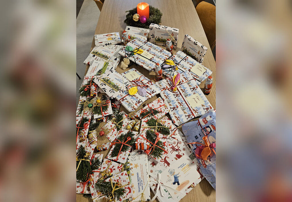 Ein Tisch voller festlich verpackter Geschenke mit einer brennenden Adventskerze.