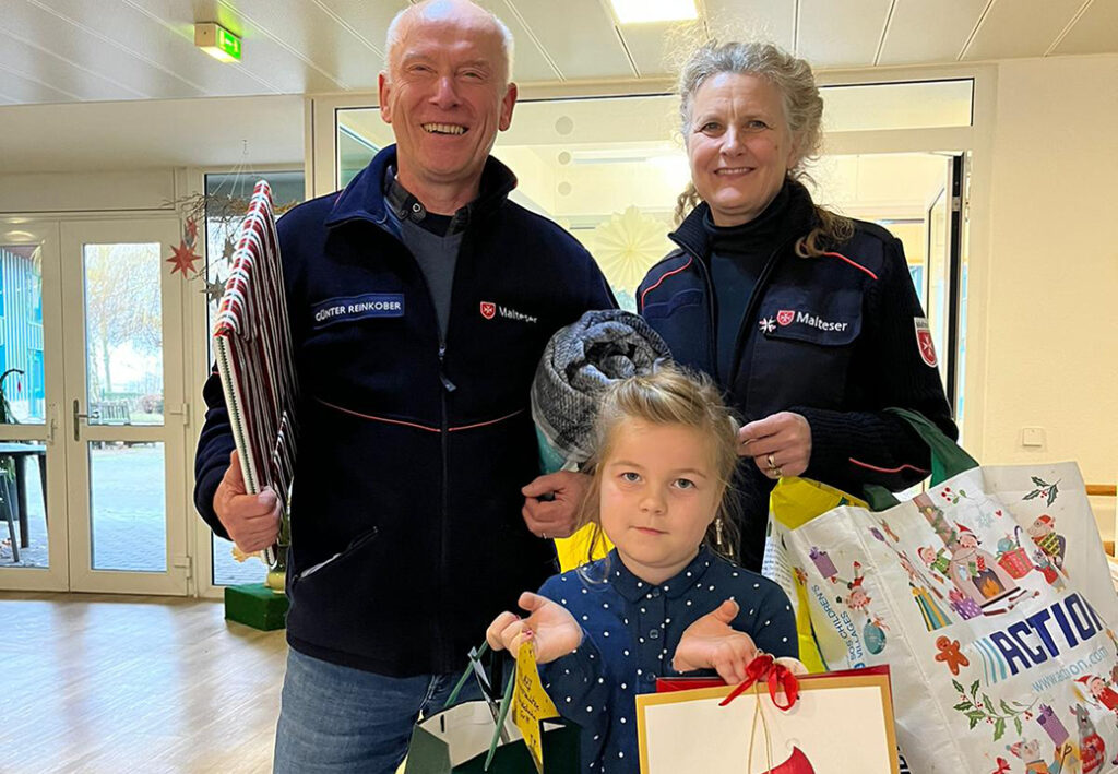 Drei Personen halten Weihnachtsgeschenke in einem Innenraum.