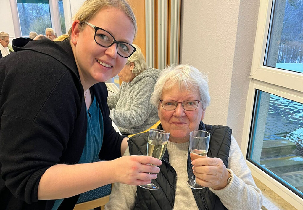 Zwei Frauen sto&szlig;en mit Sekt an, eine j&uuml;ngere und eine &auml;ltere Frau sitzen an einem Tisch.