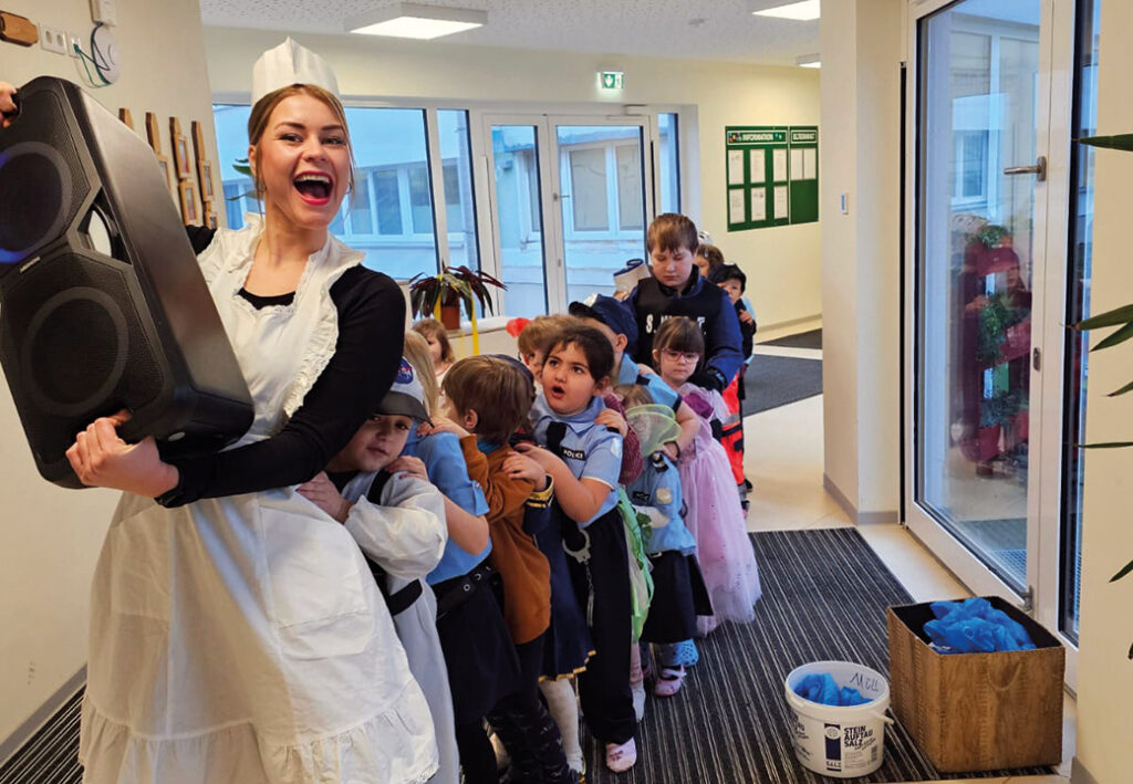 Eine fr&ouml;hliche Frau in einem Kost&uuml;m tanzt mit einer Gruppe verkleideter Kinder.