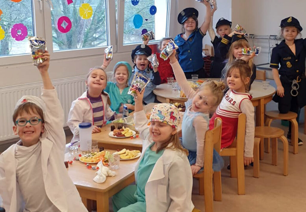 Kinder in Verkleidungen sitzen an einem Tisch und halten Fruchtsaftgetr&auml;nke hoch.