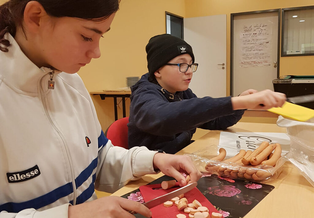 Zwei Kinder schneiden W&uuml;rstchen in einem Raum zu