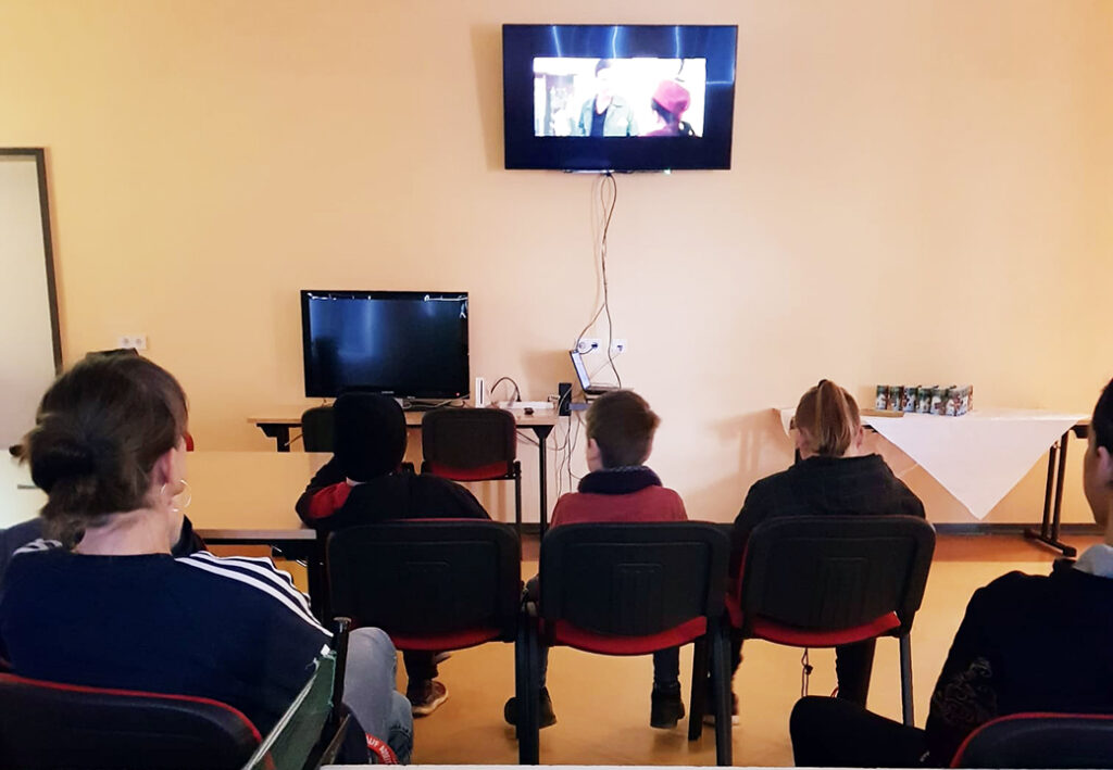 Menschen sitzen in einem Raum und schauen einen Film auf einem Wandbildschirm.