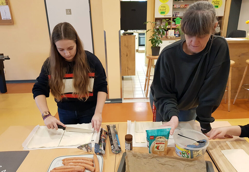Zwei Personen bei einer k&uuml;chen&auml;hnlichen Aktivit&auml;t, die Zutaten auf einem Tisch verwenden.
