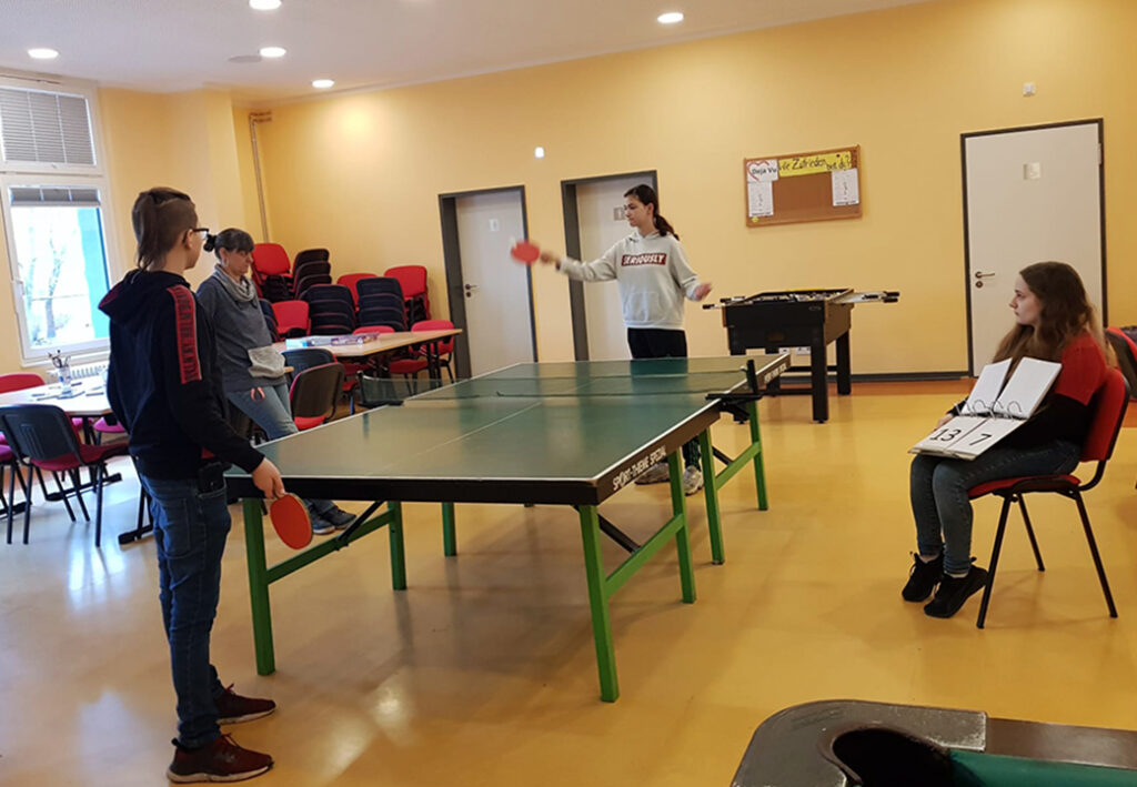 Vier Personen in einem Raum mit Tischtennistisch und Tischkicker
