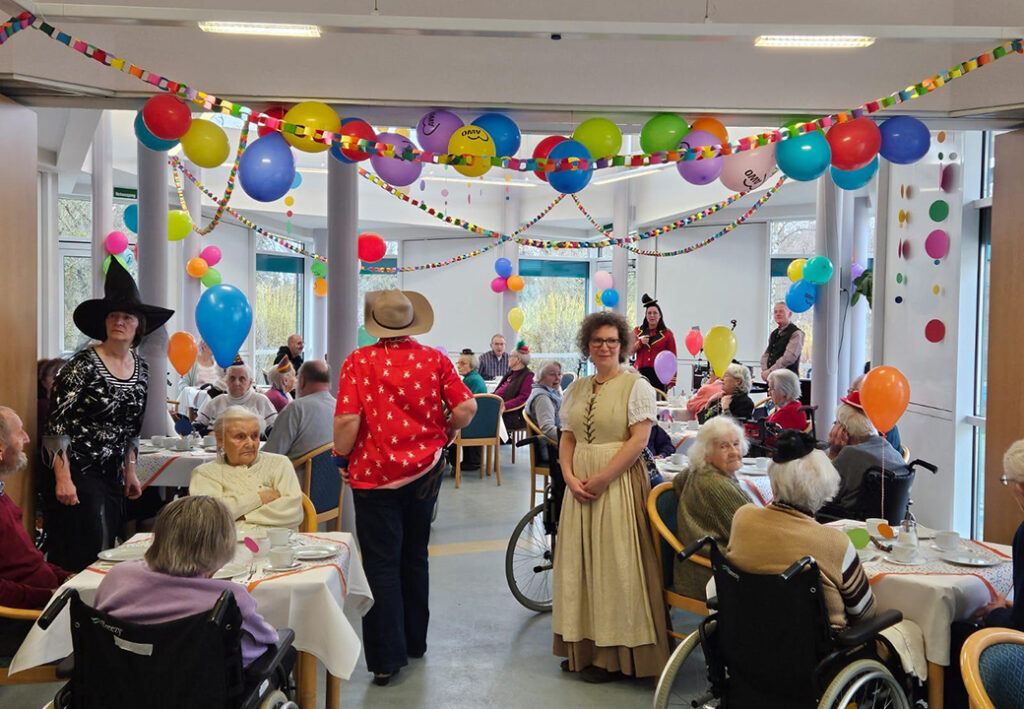 Menschen feiern in einem festlich dekorierten Raum mit bunten Ballons und Girlanden.