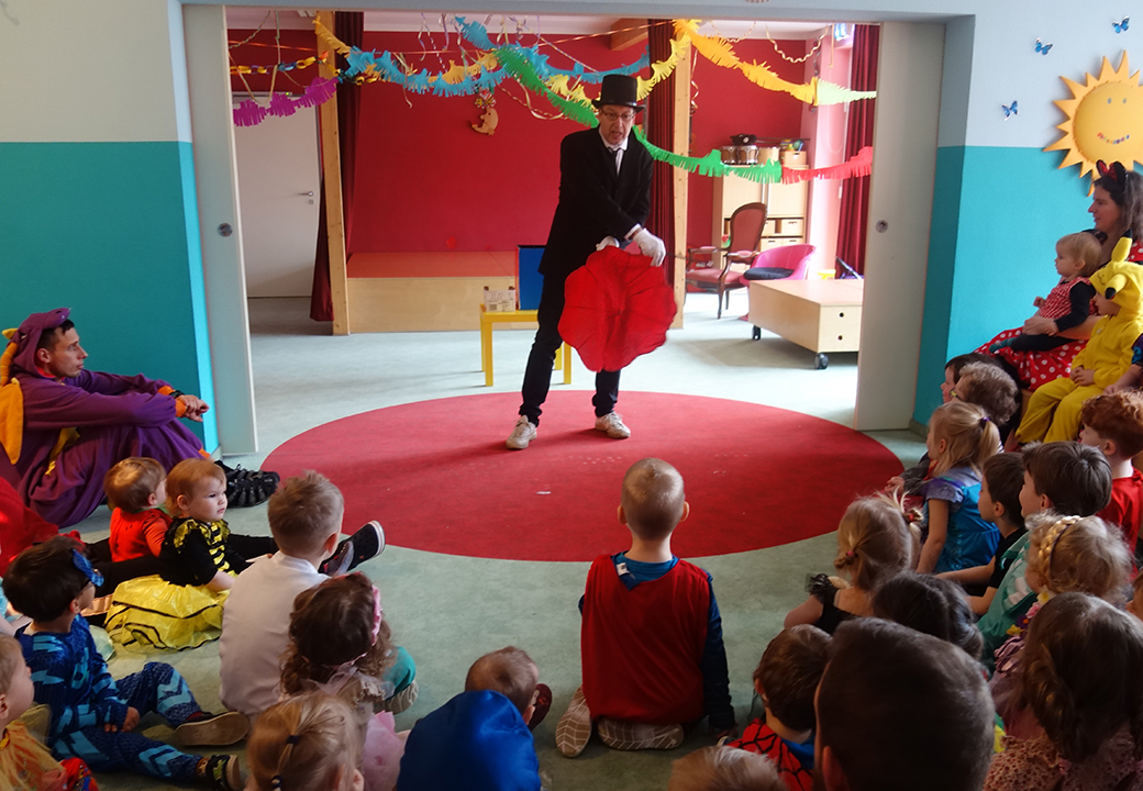 Kinder in Kostümen schauen einem Zauberer zu.