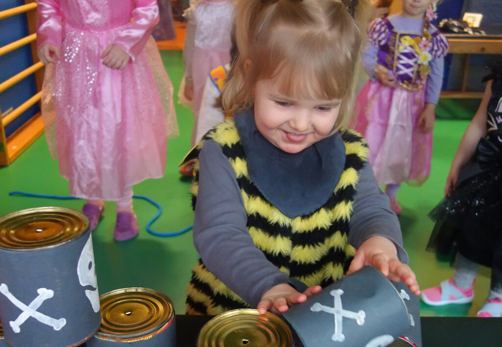 Ein Kind im Bienenkost&uuml;m spielt mit Dosen, die Totenkopf-Symbole tragen.