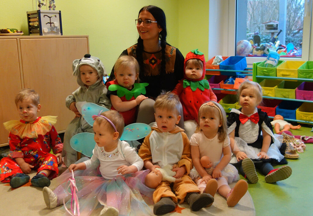 Gruppe von Kleinkindern in bunten Kost&uuml;men mit einer Betreuerin in einer Kita.