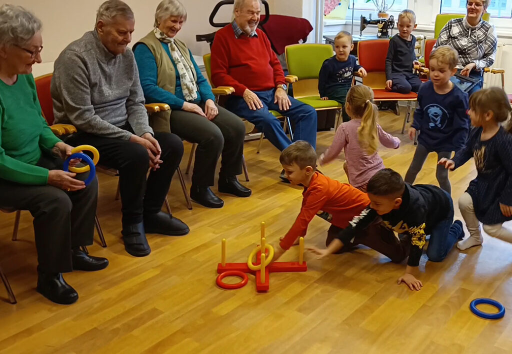 &Auml;ltere Menschen und Kinder spielen gemeinsam in einem Raum.