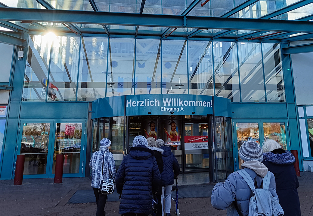 Eingang eines Einkaufszentrums mit mehreren Personen, die hineingehen