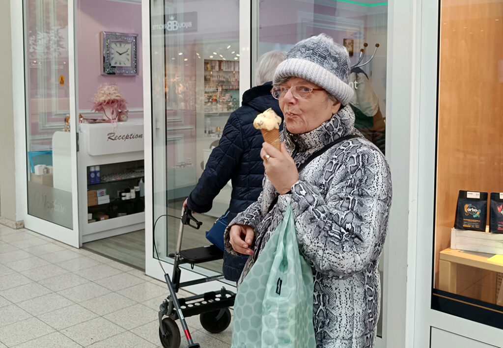 &Auml;ltere Frau in einem Einkaufszentrum, die ein Eis isst
