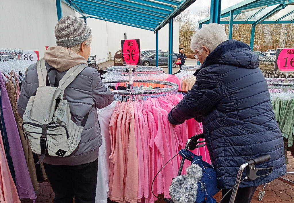 Zwei &auml;ltere Menschen beim St&ouml;bern in einem Kleiderst&auml;nder im Freien.