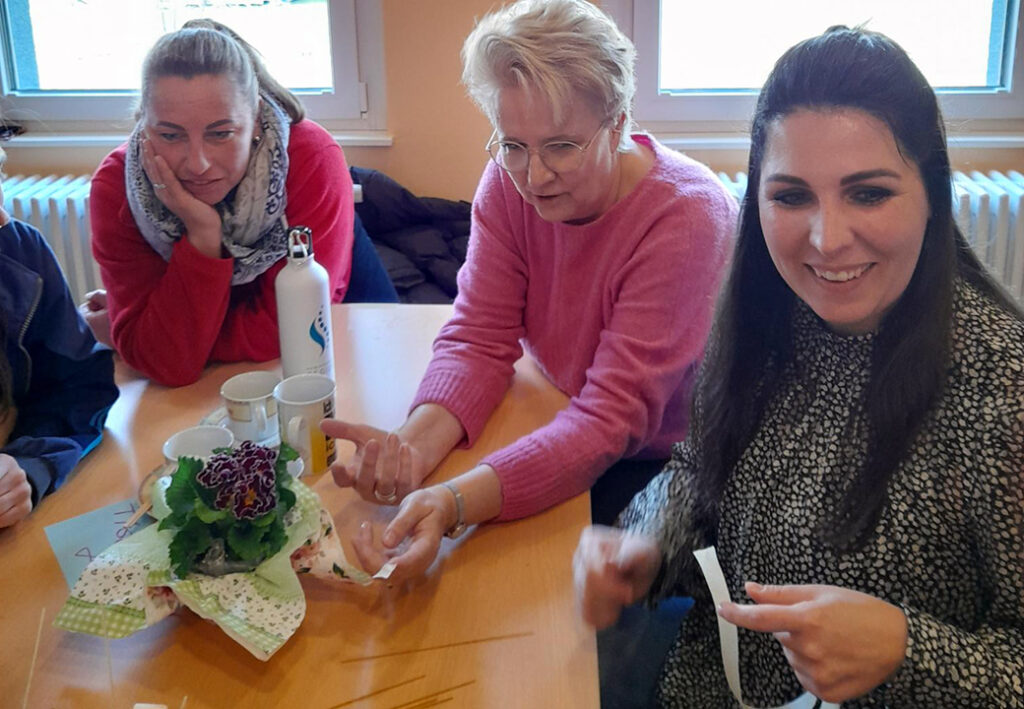 Drei Personen sitzen um einen Tisch mit Blumenarrangement.