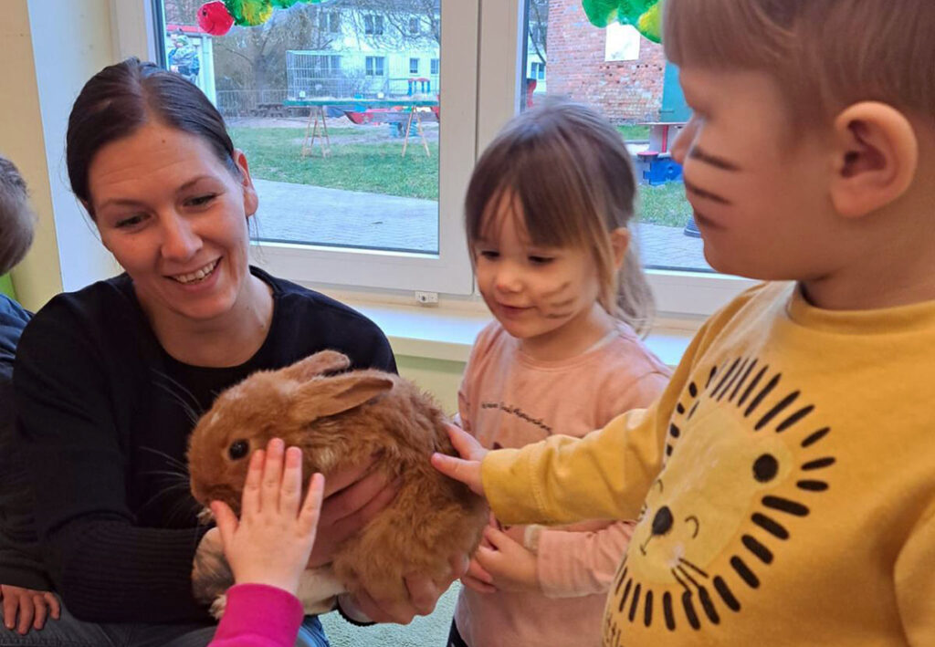 Eine Frau und Kinder streicheln ein Kaninchen in einem Raum mit Fenster im Hintergrund.