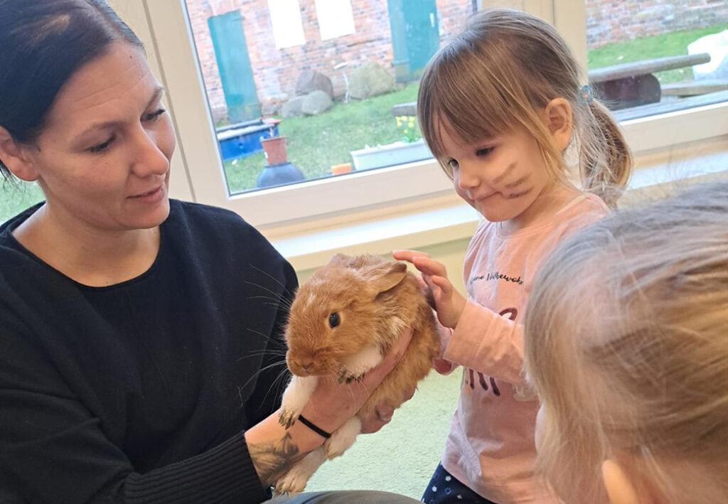 Eine Frau h&auml;lt ein Kaninchen, w&auml;hrend ein kleines M&auml;dchen es streichelt.