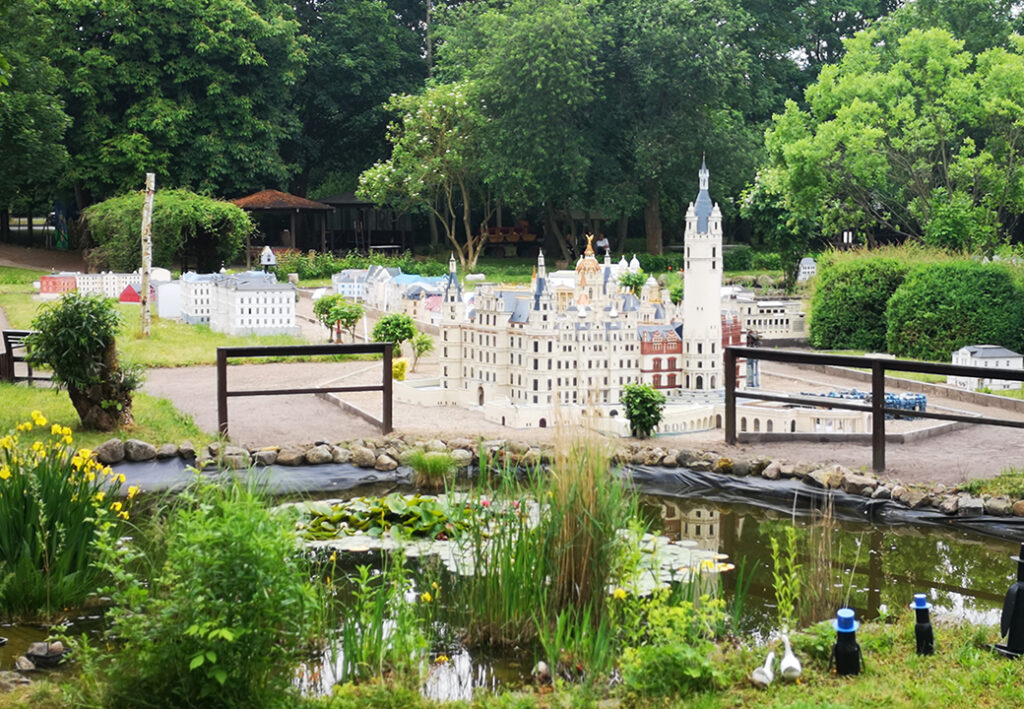 Modellpark mit Miniaturnachbildungen von Geb&auml;uden, umgeben von B&auml;umen und einem Teich im Vordergrund.