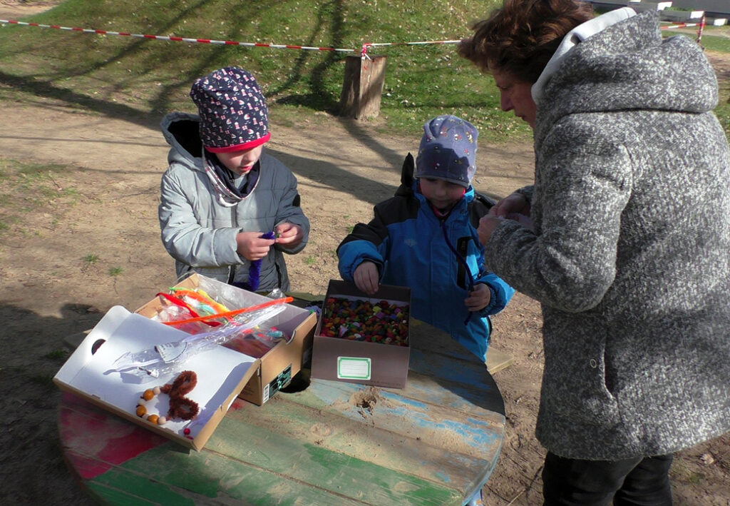 Zwei Kinder und eine erwachsene Person bei einer Bastelaktivit&auml;t im Freien