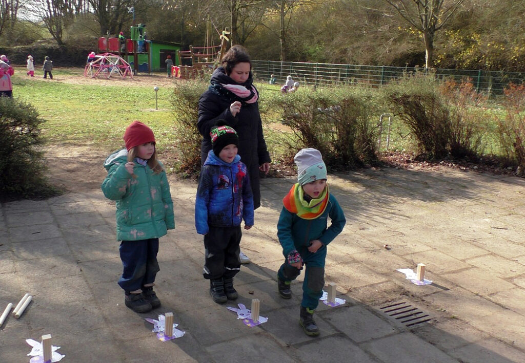 Kinder spielen im Freien mit einer Betreuerin bei k&uuml;hlem Wetter.