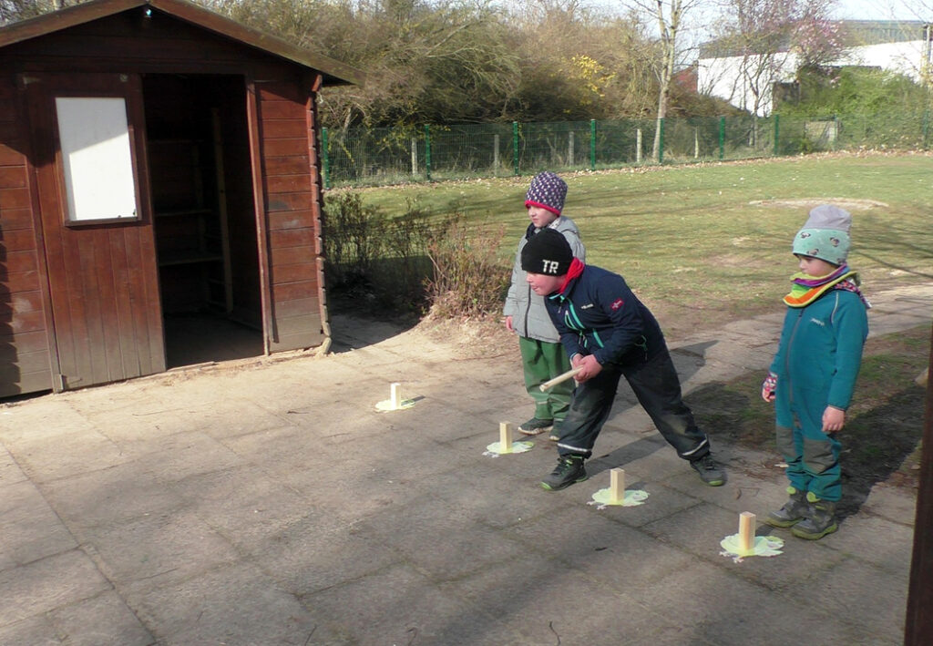 Drei Kinder spielen drau&szlig;en vor einer Holzh&uuml;tte