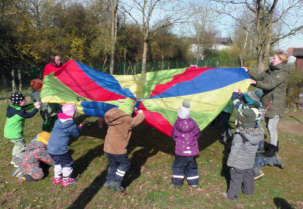 Kinder spielen mit einem bunten Schwungtuch im Freien.