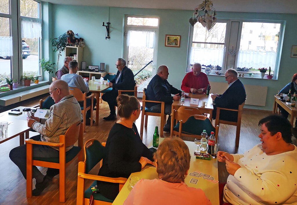 Eine Gruppe von Personen sitzt in einem Raum an Tischen und spielt Karten.