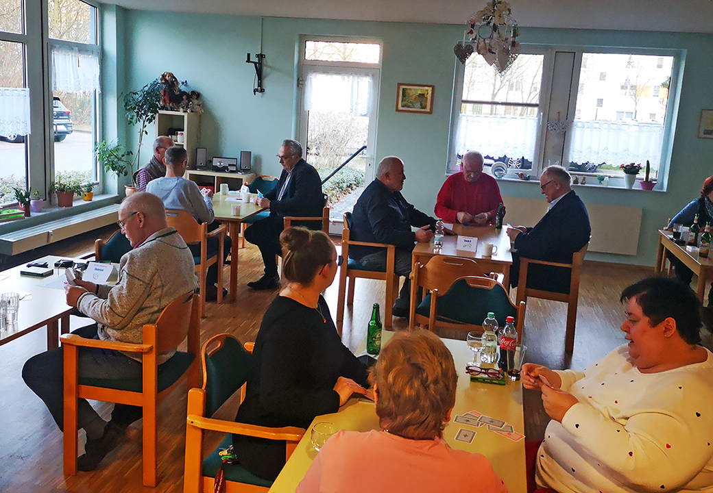 Eine Gruppe von Personen sitzt in einem Raum an Tischen und spielt Karten.