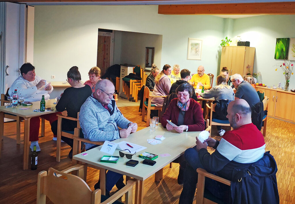 Menschen sitzen an Tischen und spielen Karten