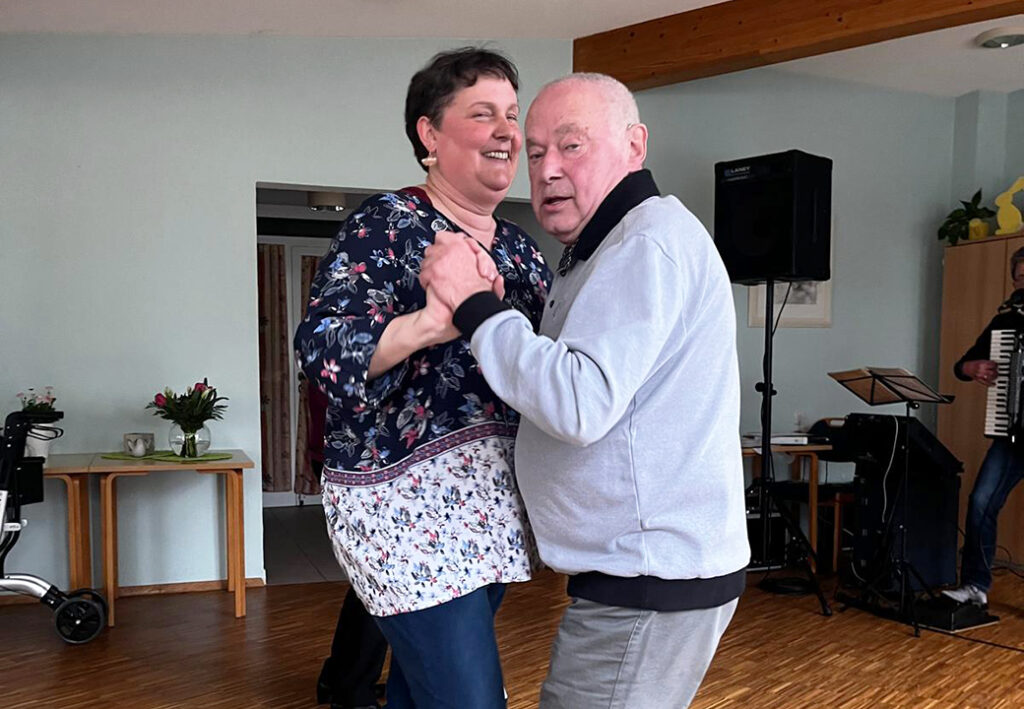 Ein &auml;lteres Paar tanzt in einem Raum mit musikalischer Begleitung im Hintergrund.