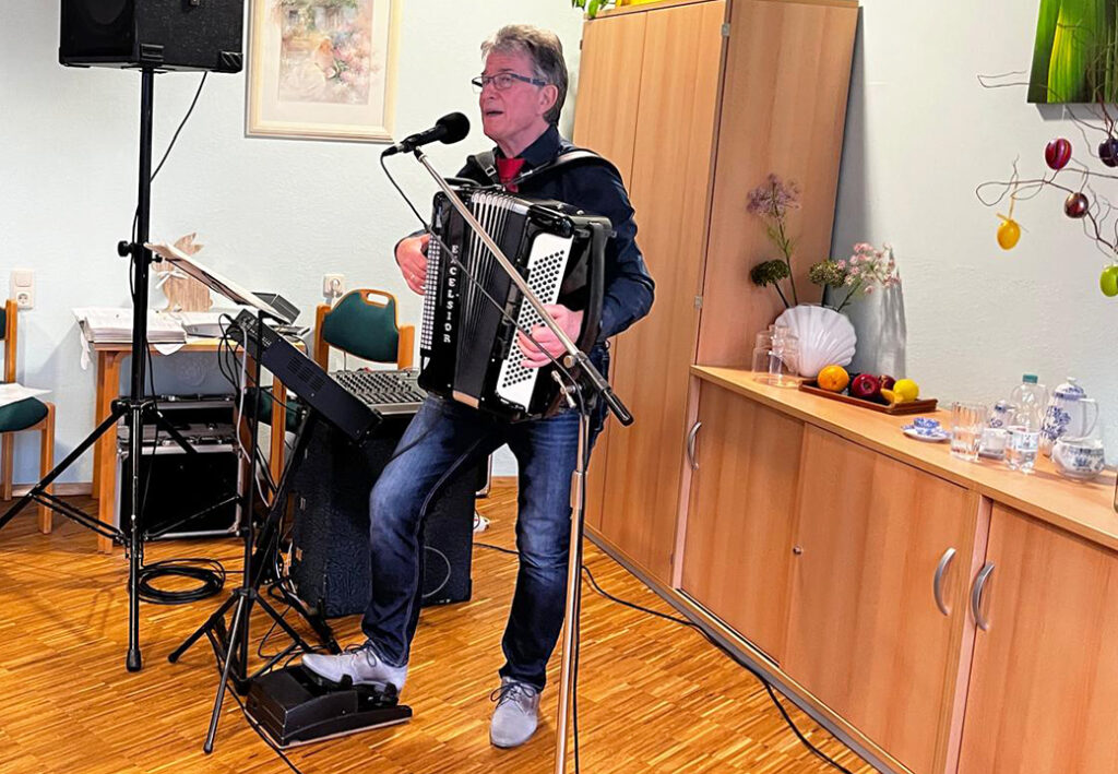 Ein Mann spielt Akkordeon und singt in einem Raum.