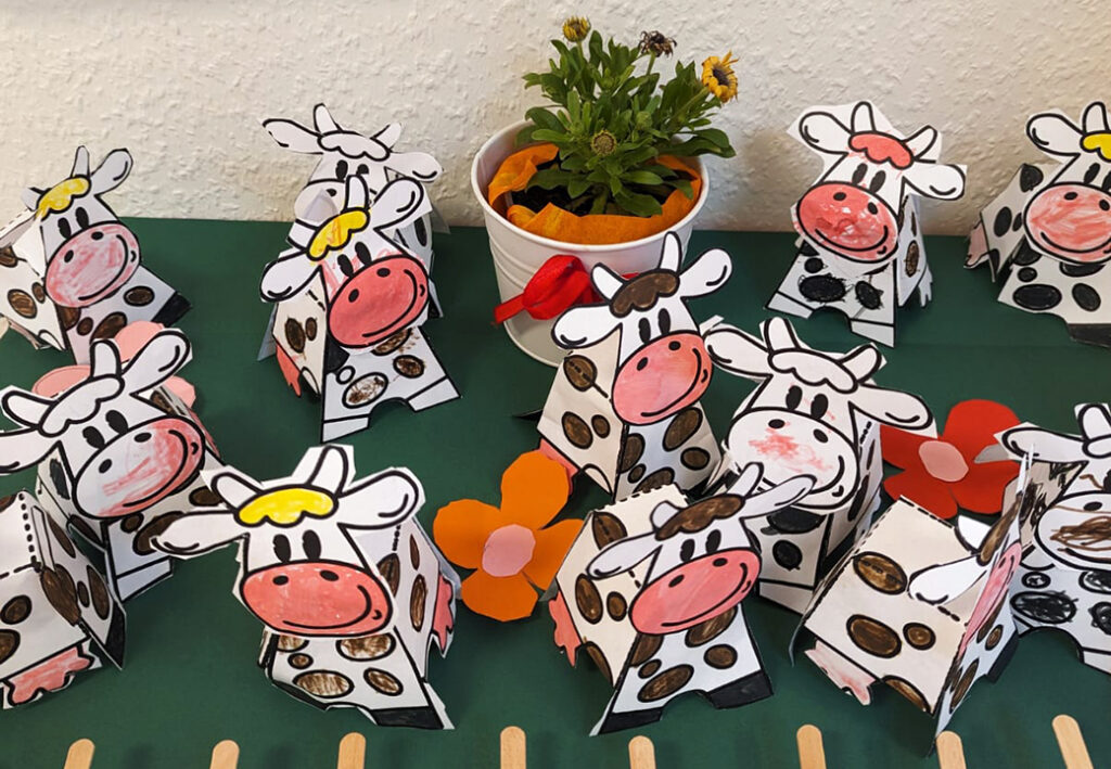 Papierfiguren von K&uuml;hen auf einem Tisch mit Blumentopf.