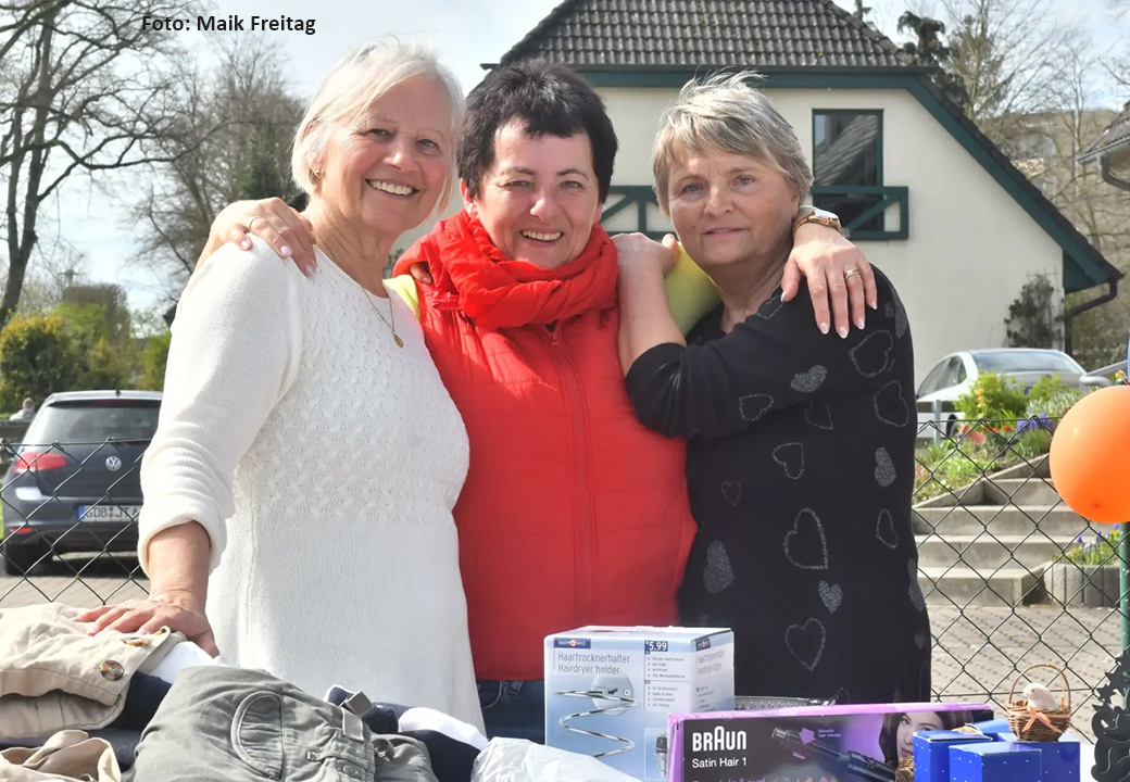 Drei Frauen stehen draußen an einem Tisch mit Haushaltsartikeln.