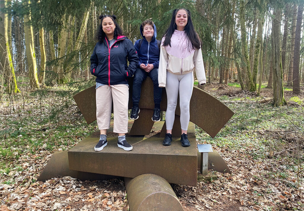Drei Personen im Wald auf einer Skulptur.