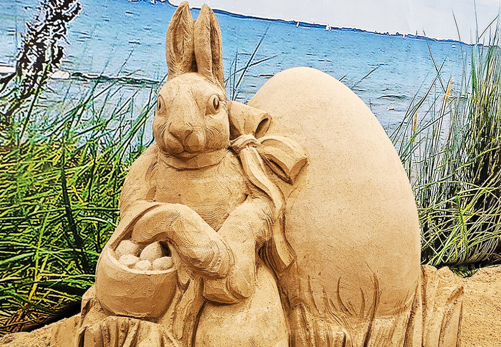 Sandskulptur eines Hasen mit Osterei am Meer