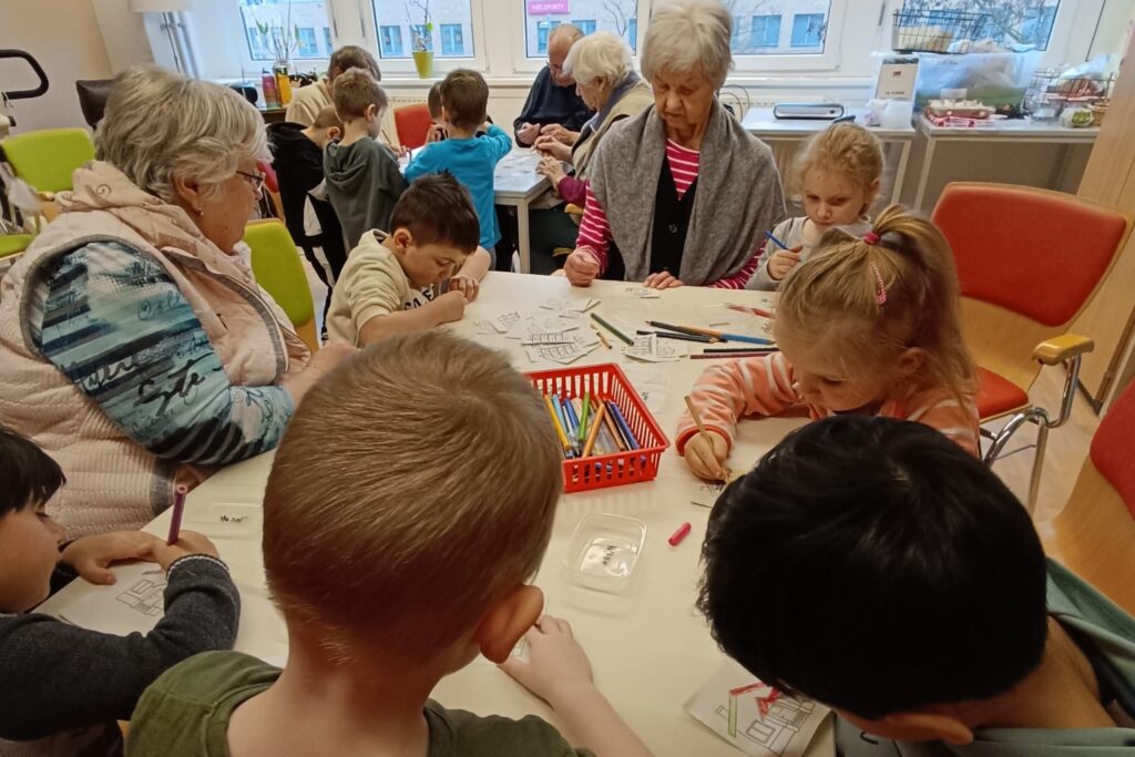 Kinder und &auml;ltere Menschen sitzen zusammen an einem Tisch und malen