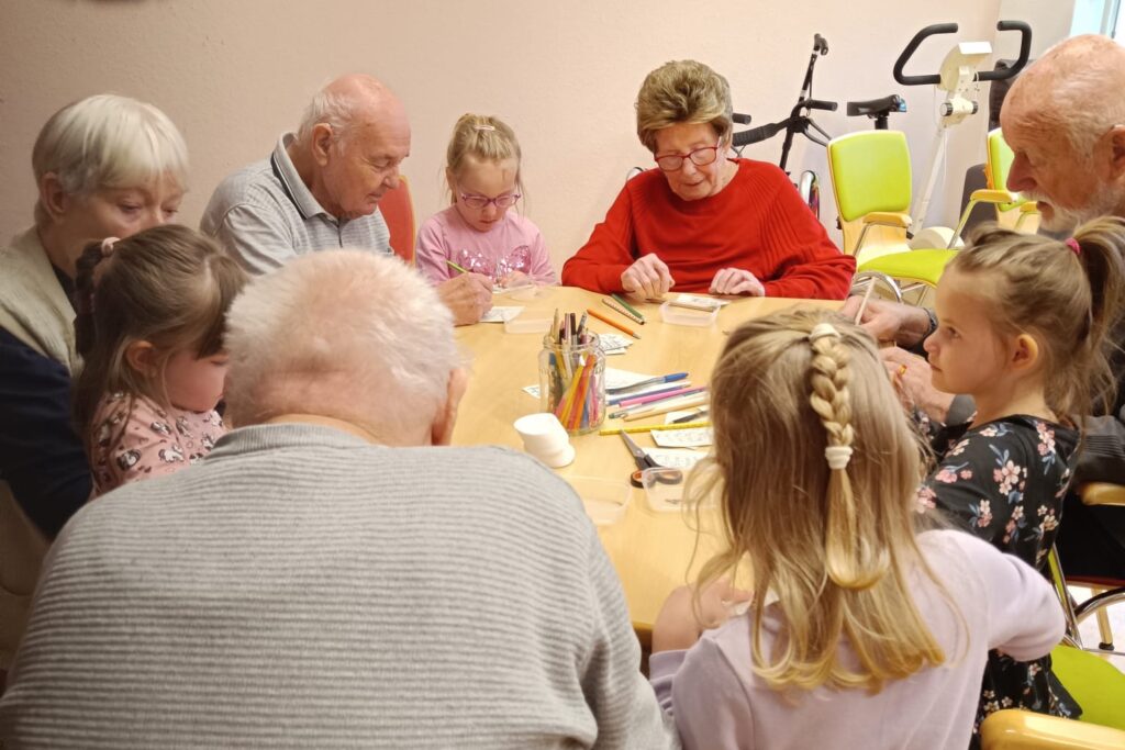 &Auml;ltere und junge Personen sitzen gemeinsam an einem Tisch und malen