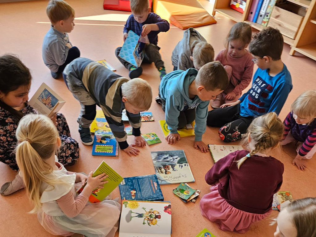 Gruppe von Kindern, die auf dem Boden sitzen und in Büchern blättern.