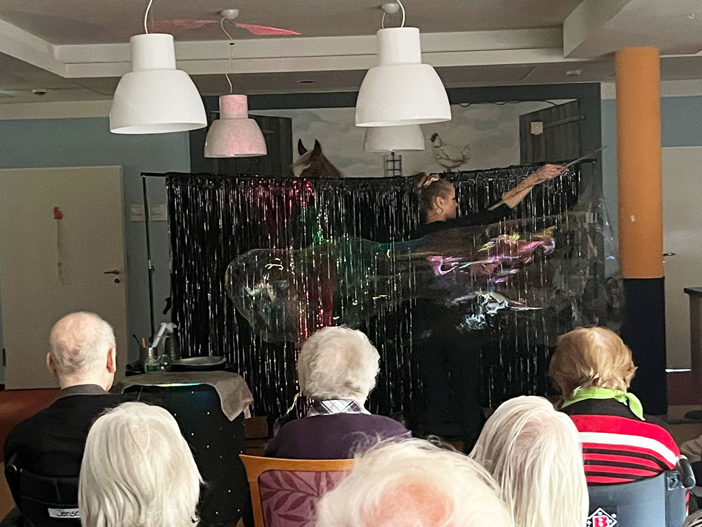 Eine Person führt eine Show mit Seifenblasen für ältere Menschen in einem Gemeinschaftsraum auf.