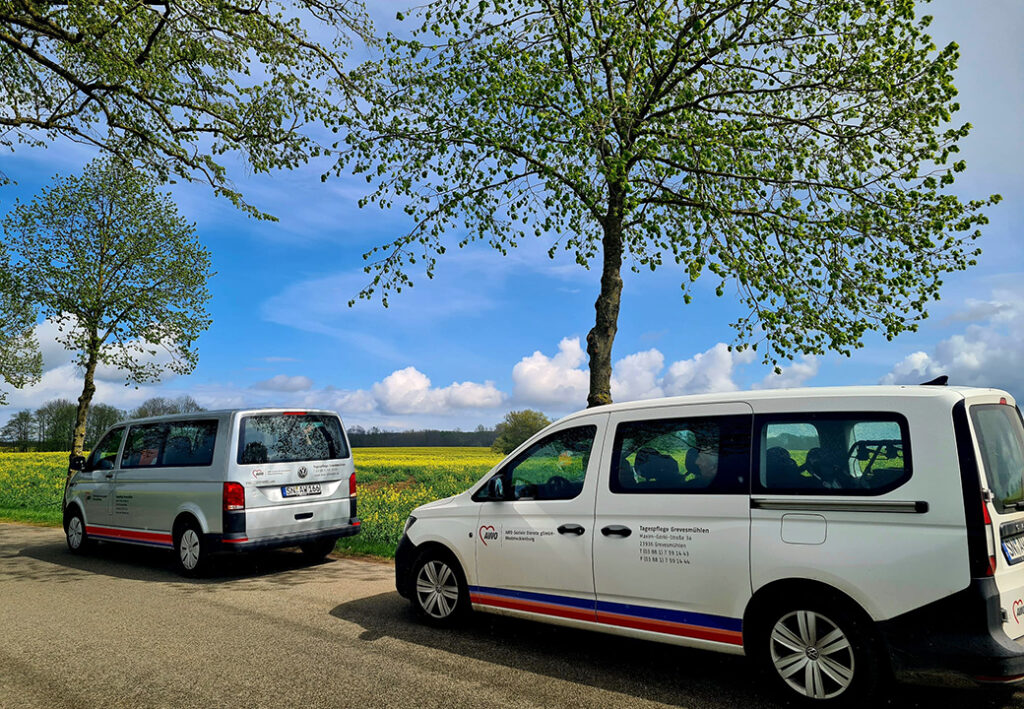 Zwei weiße AWO-Transporter parken auf einer Landstraße bei sonnigem Wetter mit blühenden Bäumen im Hintergrund.