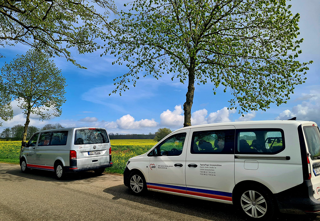Zwei weiße AWO-Transporter parken auf einer Landstraße bei sonnigem Wetter mit blühenden Bäumen im Hintergrund.