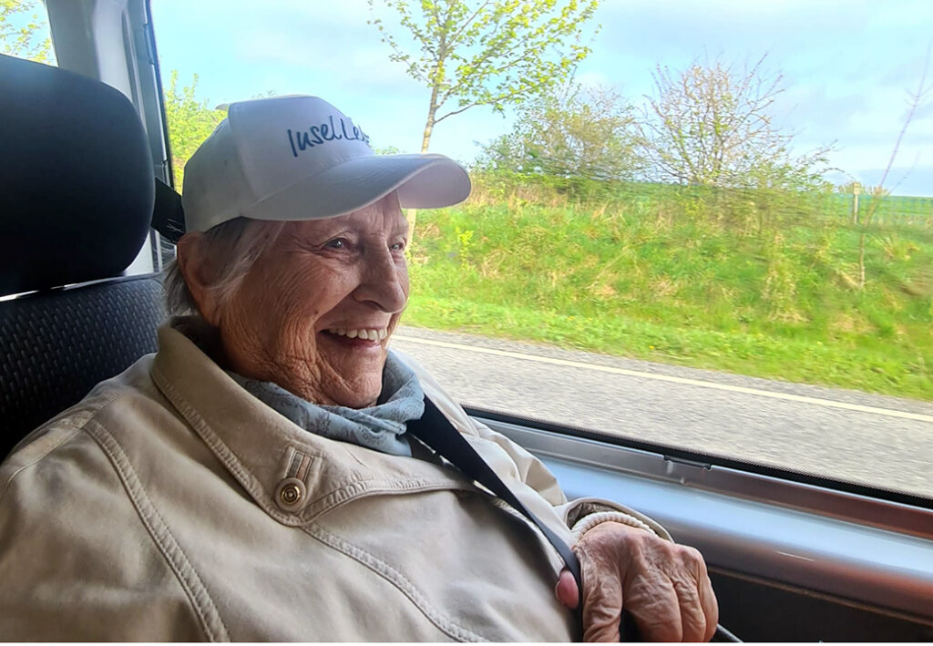 &Auml;ltere Frau im Auto, l&auml;chelnd mit wei&szlig;er Kappe.