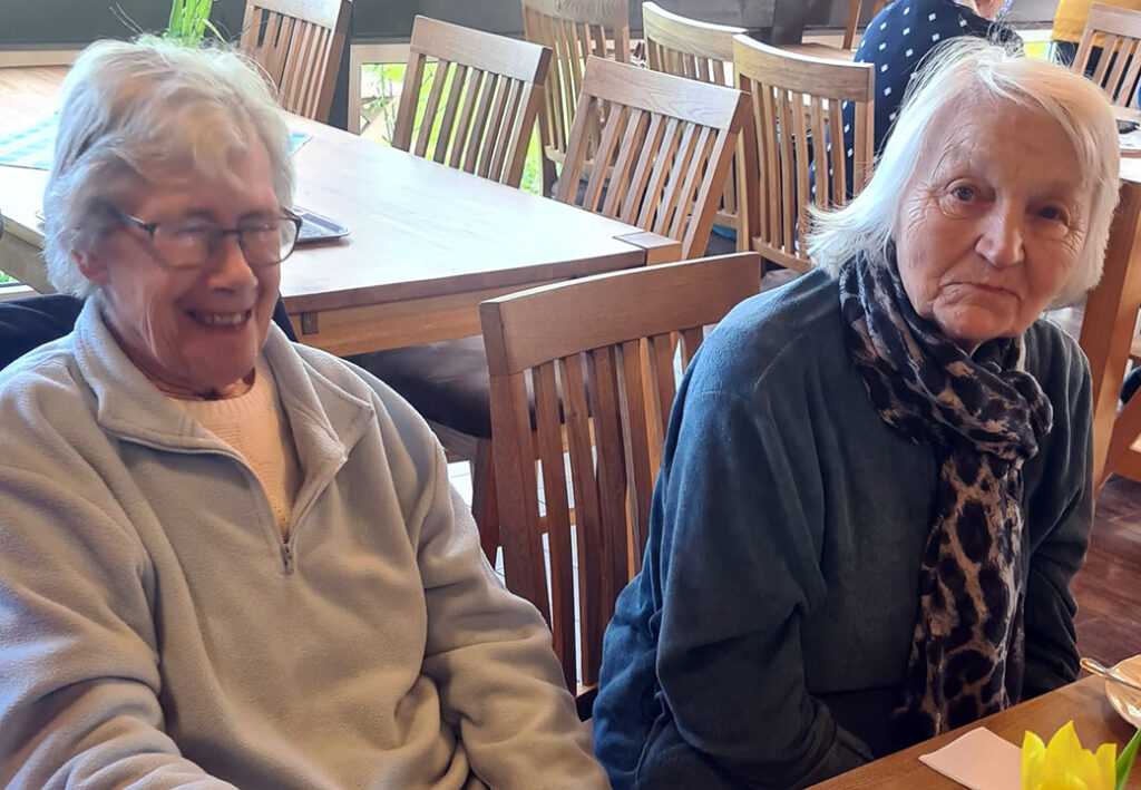 Zwei &auml;ltere Frauen sitzen an einem Tisch in einem Gemeinschaftsraum.