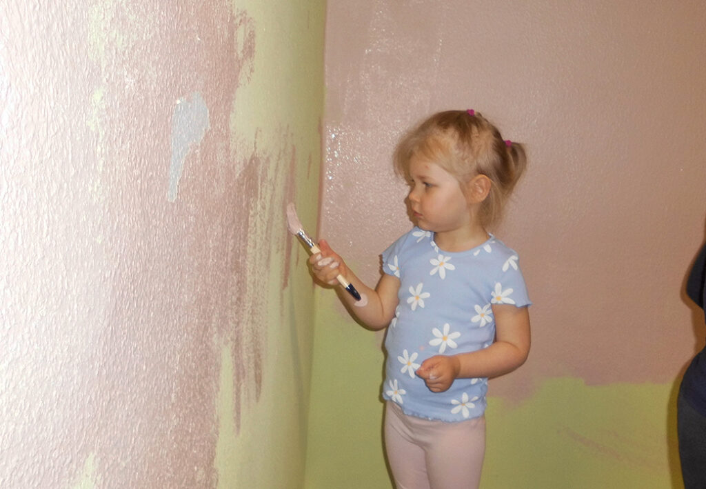 Ein kleines Mädchen malt mit einem Pinsel an einer Wand